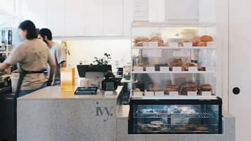 A bakery counter with pastries and a coffee machine, a person working behind the counter, and a display case with baked goods.