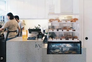 Un comptoir de boulangerie avec des pâtisseries et une machine à café, une personne qui travaille derrière le comptoir, et une vitrine remplie de produits de boulangerie.