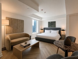 Een moderne hotelkamer met een groot bed, een bank, een bijzettafeltje met boeken, een nachtkastje en uitzicht over de stad.
