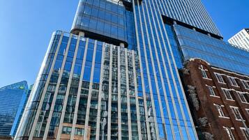 A modern skyscraper with a glass facade, a prominent entrance with a canopy, and a parking area with vehicles.