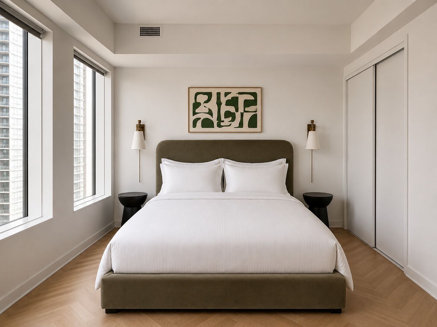 Une chambre moderne avec un grand lit, deux tables de chevet, une œuvre d’art accrochée au mur et une vue sur un immeuble par la fenêtre.