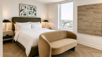 Une chambre moderne avec un lit, des lampes de chevet, une fenêtre donnant sur la ville et un grand tableau abstrait.