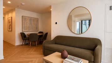 A modern living room with a sofa, a coffee table, a dining area with chairs, and a large mirror on the wall.