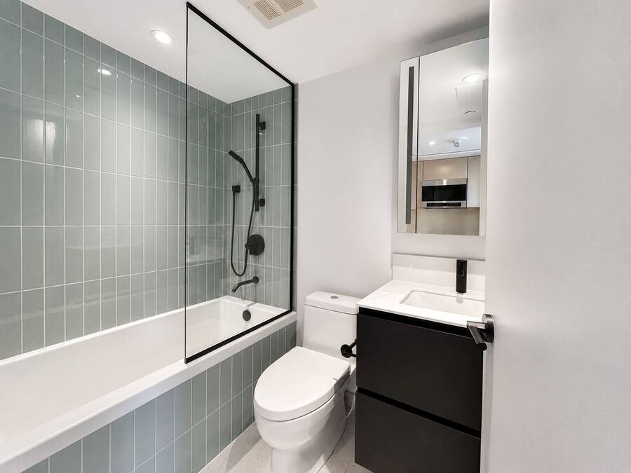 Un baño moderno con ducha envuelta en vidrio, inodoro blanco y mueble negro.