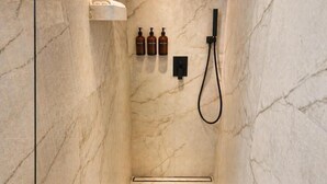 A bathroom with a marble wall, a handheld showerhead, and three bottles of shampoo. - Modern Elegance & Old-World Charm in the Most Iconic District – 623 (Budapest)
