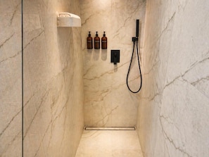 Ein Badezimmer mit Marmorwand, Duschbrause und drei Shampoo-Flaschen.
