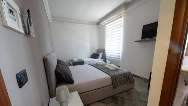 A small, compact bedroom with a single bed, bedside table, and a mounted TV.