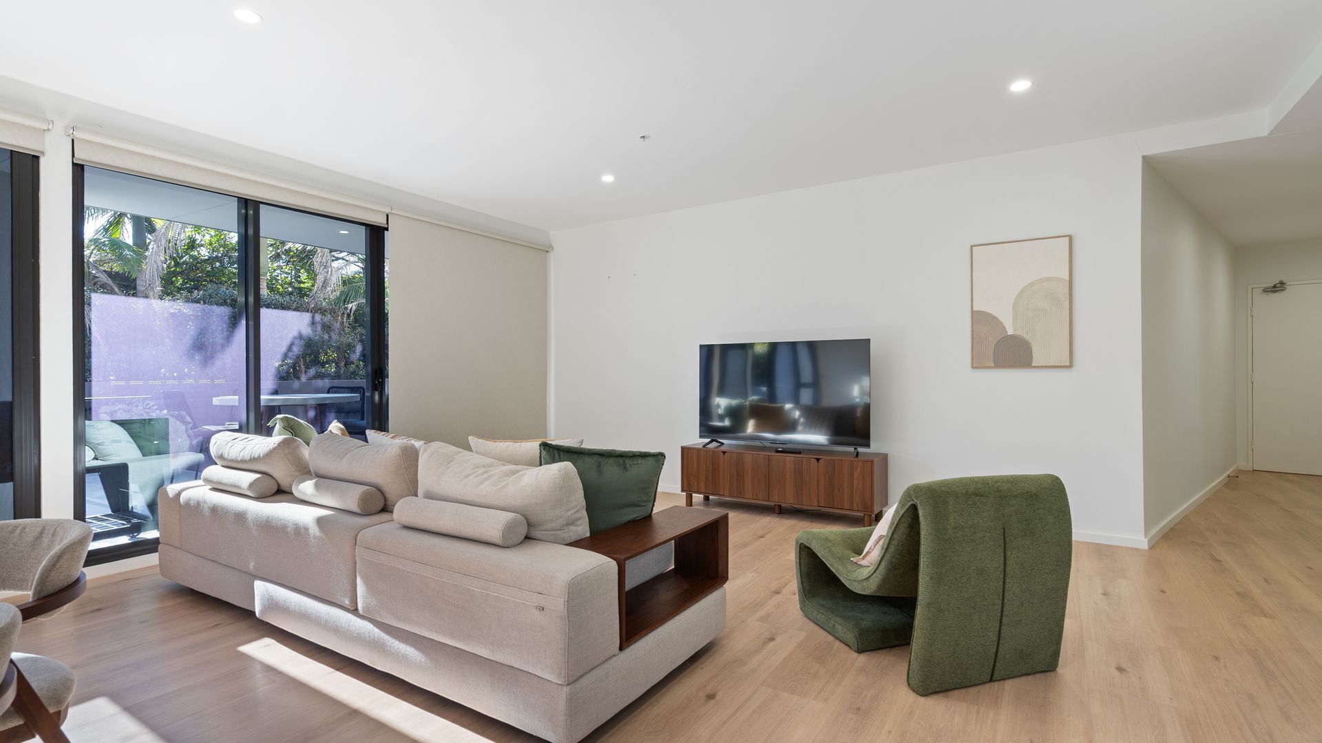 Un salon moderne avec un canapé, un téléviseur et un fauteuil vert.