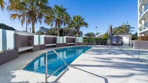 Ein Swimmingpool mit klarem, blauem Wasser, umgeben von einem modernen Gebäude mit Glasgeländern und Palmen.