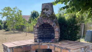 Ein Backstein-Grill im Freien mit Schornstein, umgeben von Gras und Bäumen.