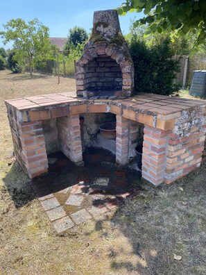 Ein Backstein-Grill im Freien mit Schornstein, umgeben von Gras und Bäumen.