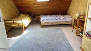 Ein kleines Schlafzimmer im Dachgeschoss mit zwei Etagenbetten, einem Dachfenster, einem Bücherregal und Teppichboden.