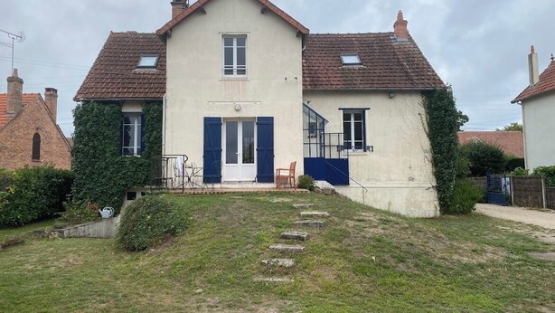 Ein zweistöckiges Haus mit Eingangstür, einer kleinen Veranda und einer sichtbaren Treppe, die zum Obergeschoss führt.