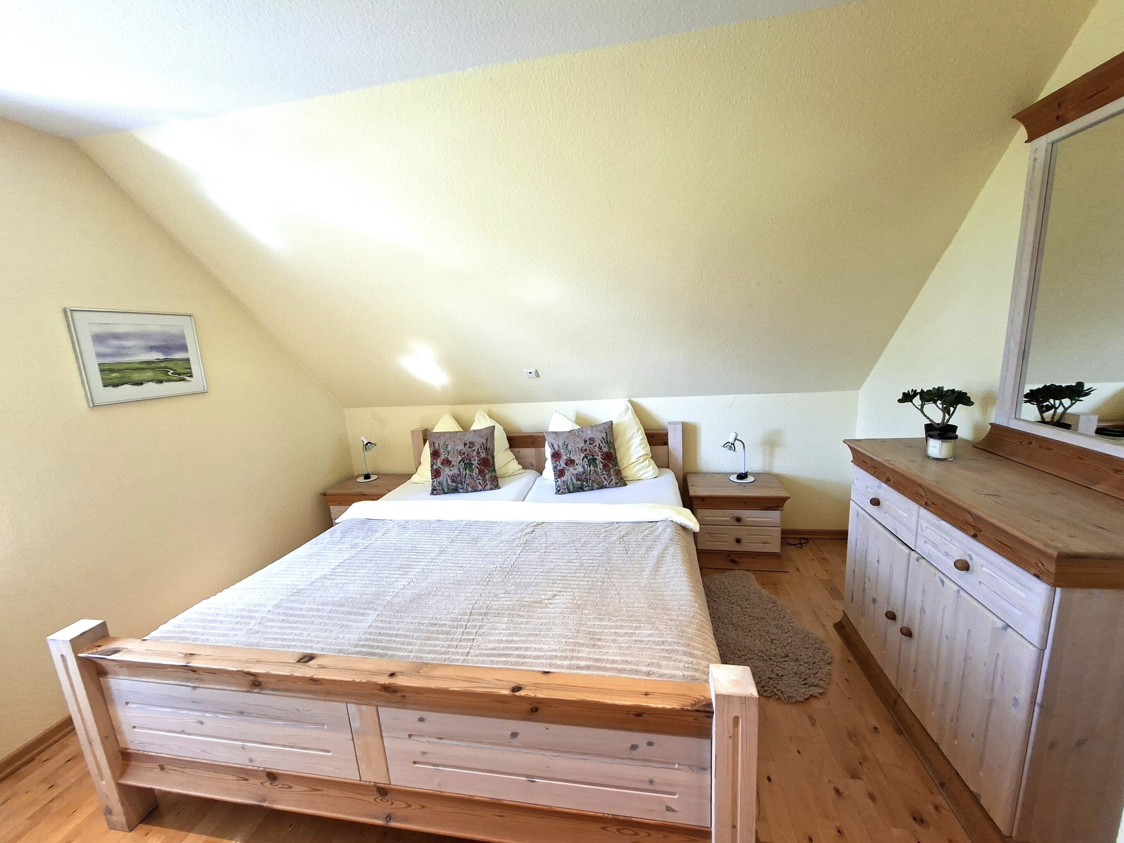 A bedroom with a wooden bed, two bedside tables, a nightstand, a dresser, and a mirror.