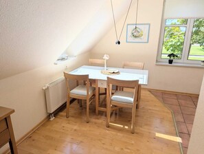 A dining area with a white table and chairs, a radiator, and a window with a plant. - Luxury "Lachmöwe" Vacation Rental in Haus Wattenblick (Warwerort)