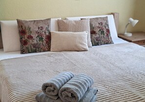 A neatly made bed with a textured bedspread, two pillows with floral patterns, and two rolled towels on the bed. - High-quality "Strandläufer" vacation rental in Haus Wattenblick with its own sauna (Warwerort)