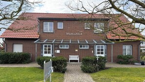 En bygning af mursten med rødt tegltag, en hvid bænk og en sti, der fører til indgangen.