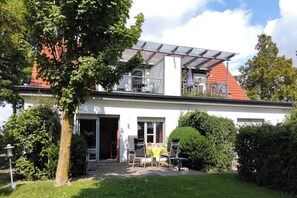 Ein zweistöckiges Haus mit einer überdachten Terrasse, einer Garage und einem gepflegten Garten.