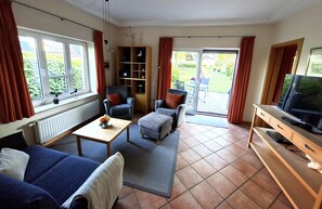 A living room with a sofa, armchair, ottoman, coffee table, television, and a bookshelf. - A Comfortable Vacation: The High-Quality "Austernfischer" Vacation Rental in Warwerort (Warwerort)