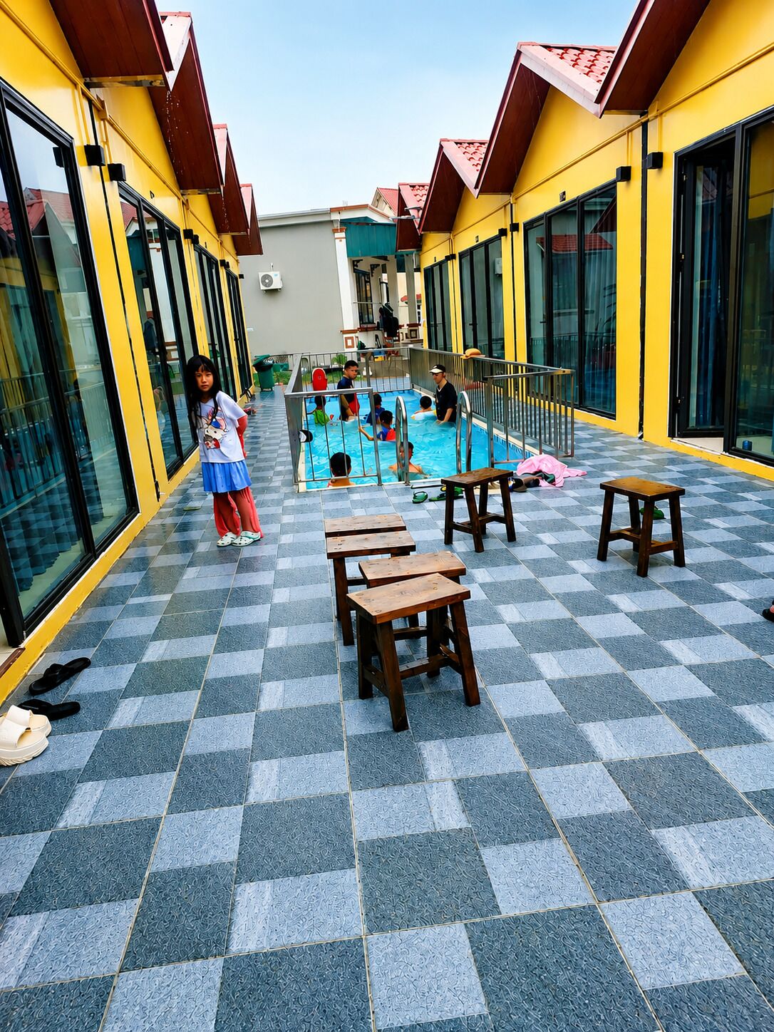 A pool area with tiled flooring, benches, and a person standing by the pool.