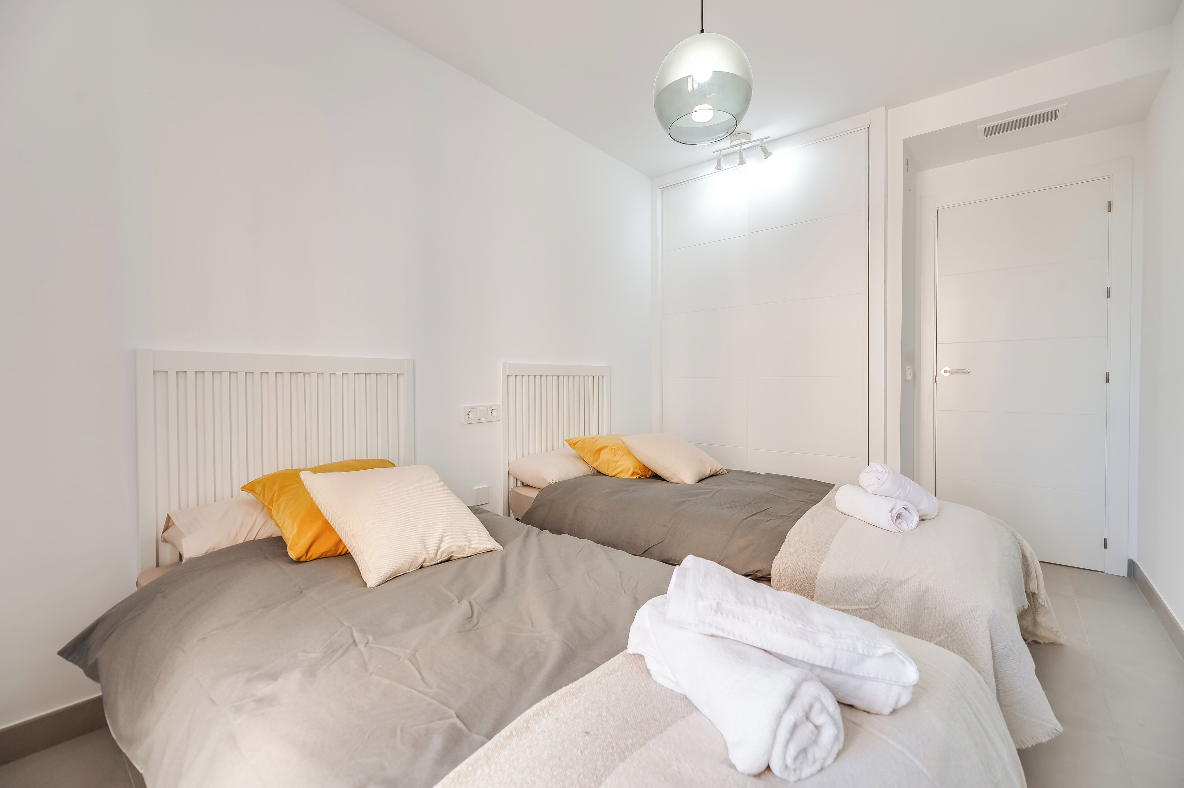 Quarto de hotel com duas camas, um radiador, uma porta e um candeeiro suspenso.