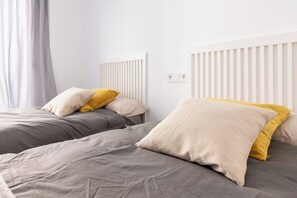 Quarto de hotel com duas camas, cada uma com roupa de cama cinzenta e almofadas amarelas.