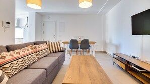 A modern living room with a sofa, a wooden coffee table, and a dining area with chairs. - LXR Lombok 2-Bedroom by the Sea (Fuengirola)