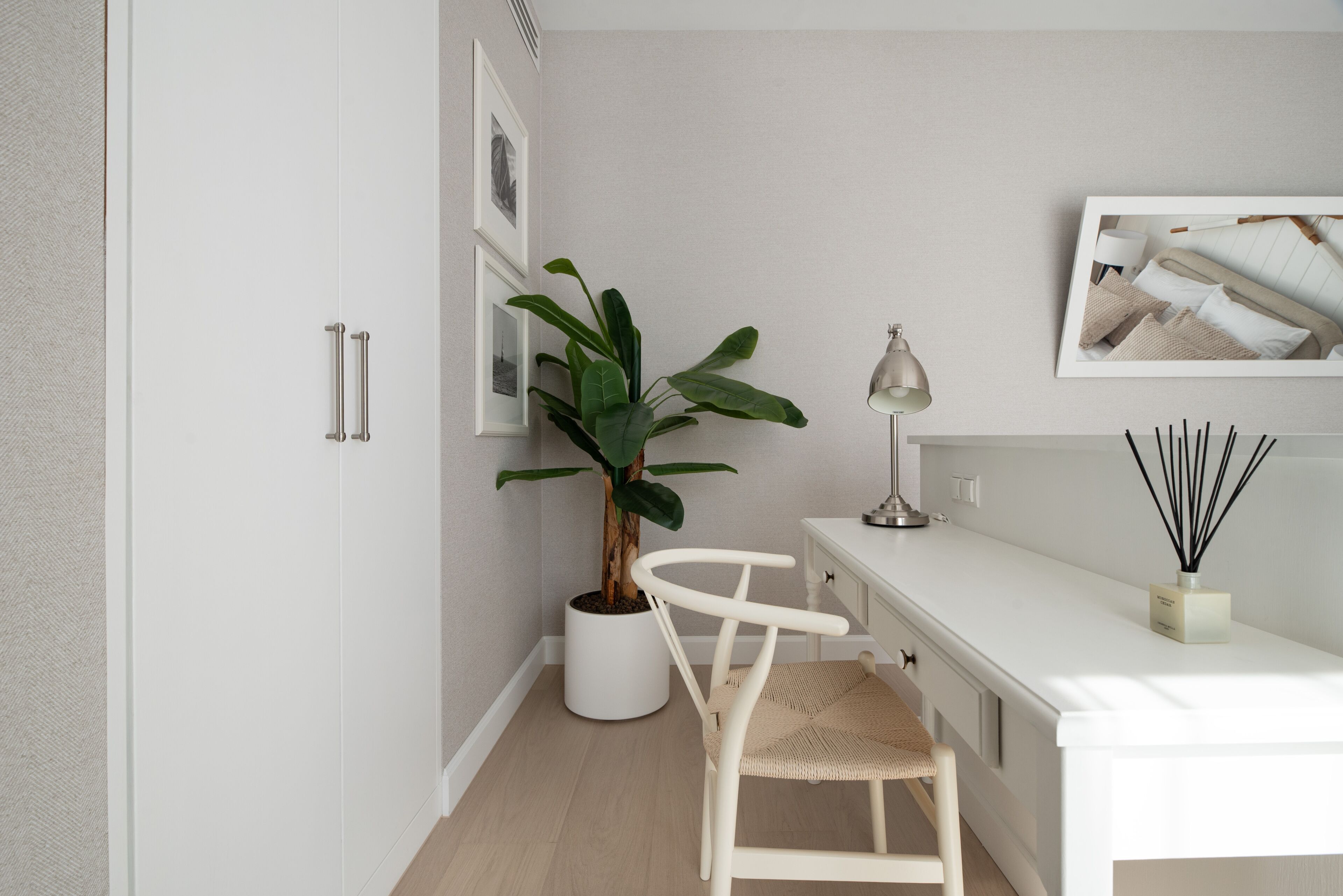 Une pièce moderne et minimaliste, avec un bureau blanc, une plante en pot, une chaise et des éléments de décoration fixés au mur.