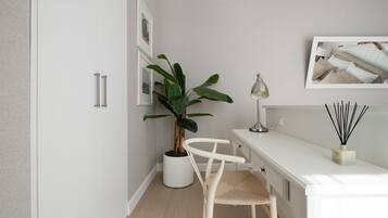 Et moderne, minimalistisk værelse med et hvidt skrivebord, en potteplante, en stol og dekoration på væggen.