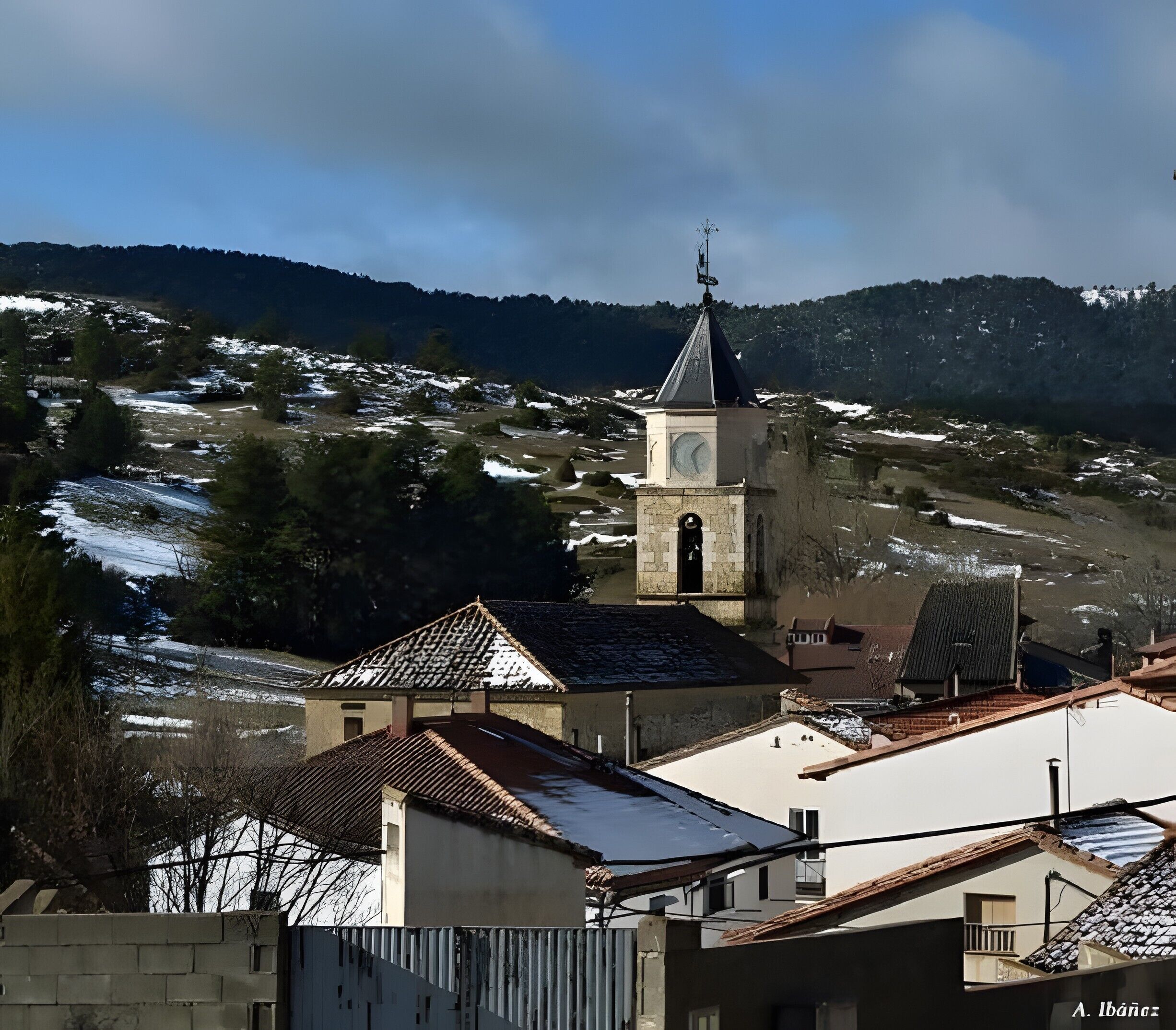 A rural landscape with a church tower, a river, and snow-covered hills.