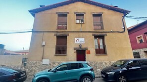 Un edificio de dos pisos con un cartel que indica 'La Galera'. Hay dos autos estacionados adelante, y el edificio tiene una puerta roja y ventanas con barrotes.