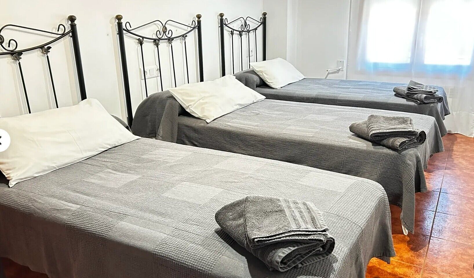 A room with two single beds with metal frames, grey bedding, and a wooden floor.