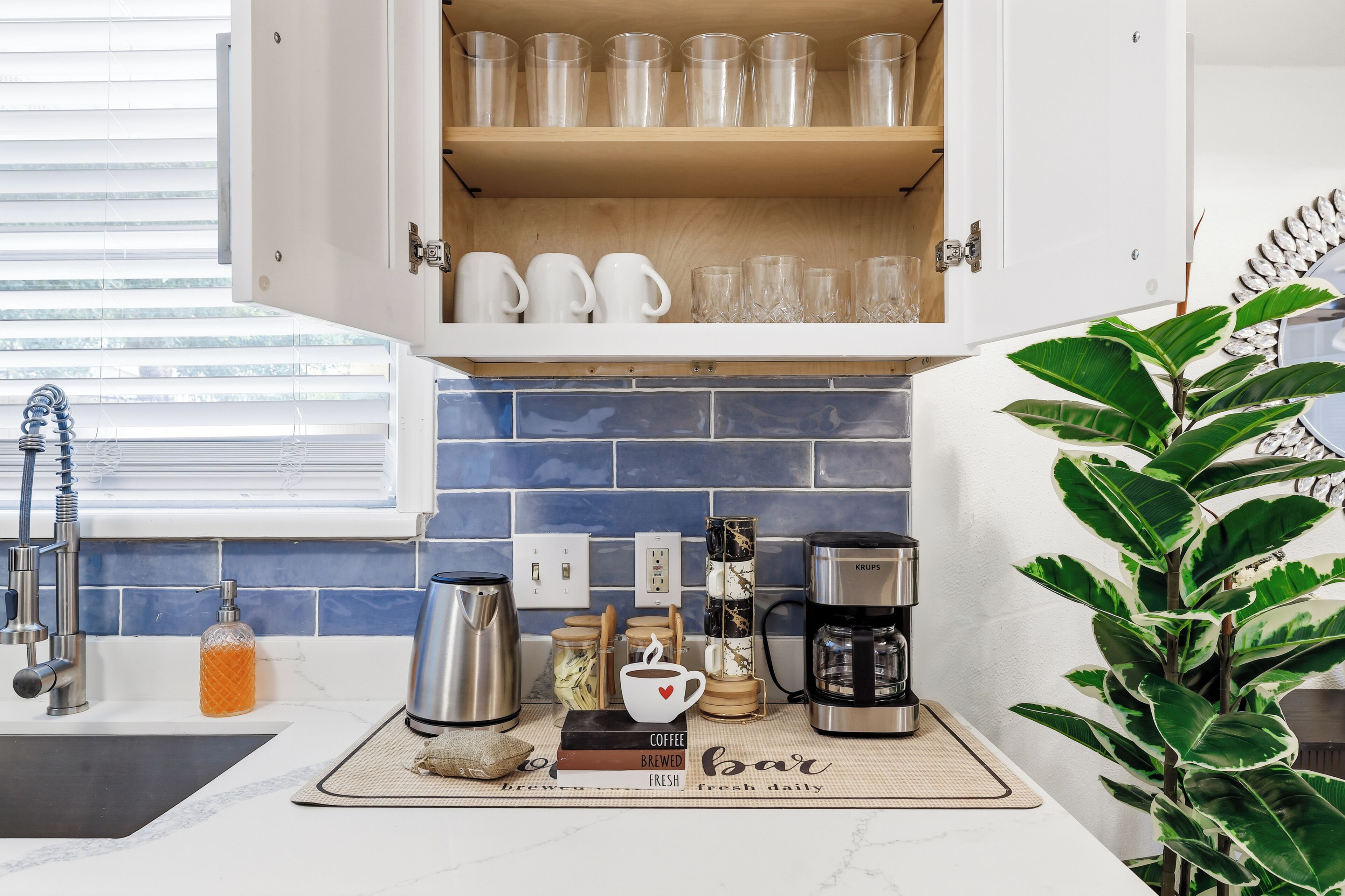 Una cocina con estación de café, que incluye una cafetera Krups, una taza de café y un molinillo de granos de café.