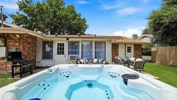 Un patio trasero con jacuzzi, una parrilla y un porche con mobiliario exterior.