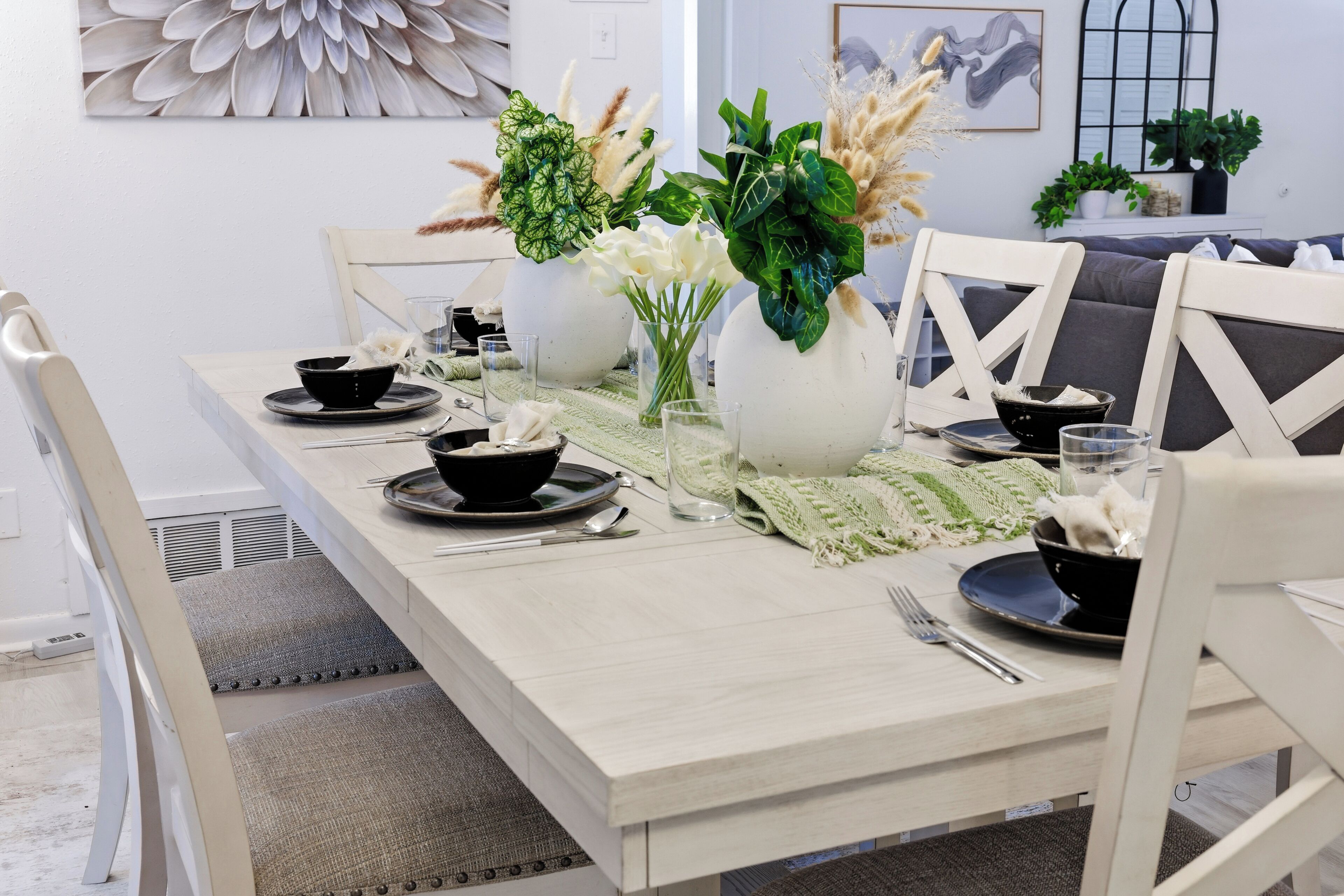 Mesa lista con cuencos, platos y cubiertos negros, rodeada de sillas blancas.