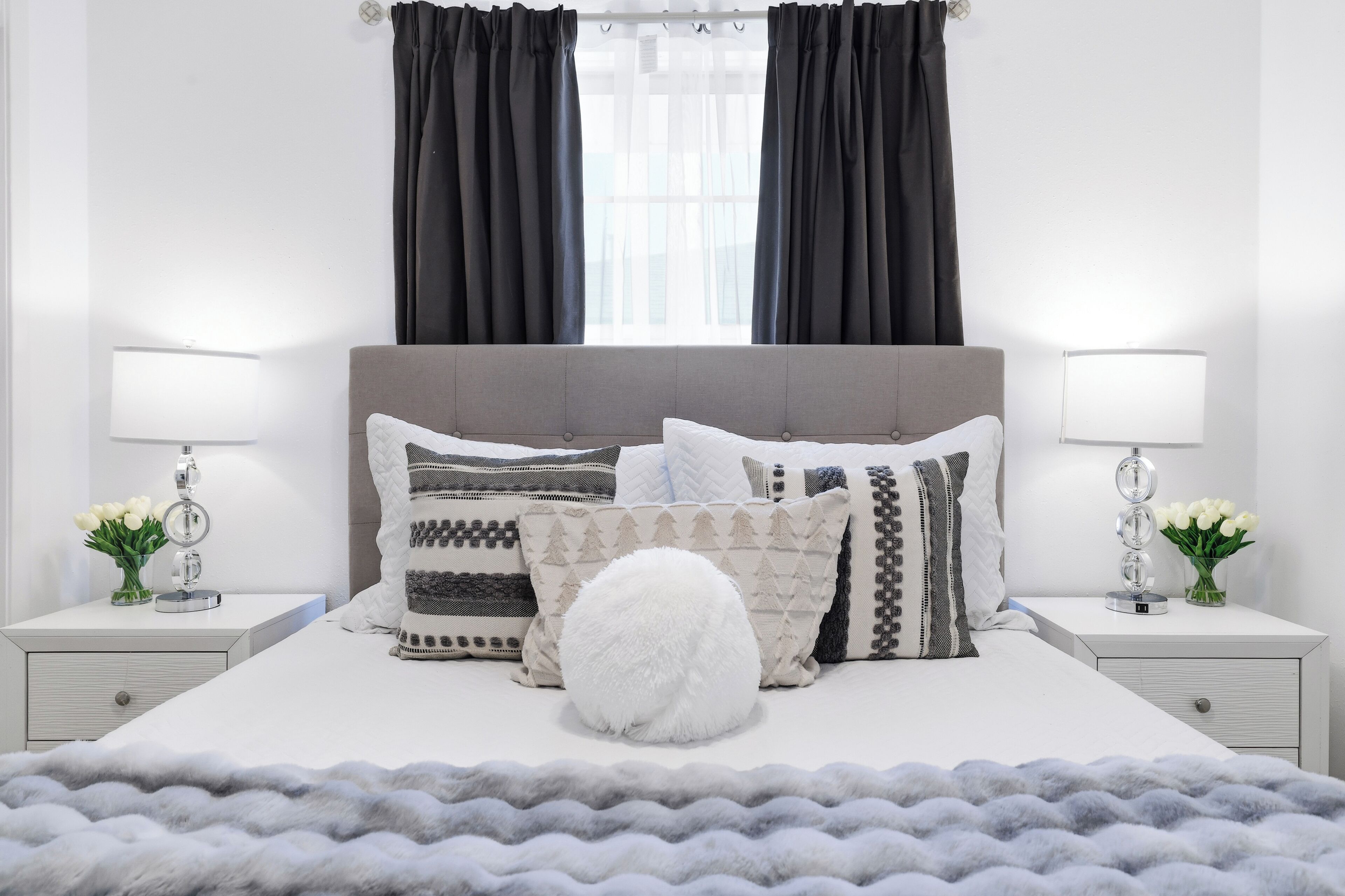 Un dormitorio ordenado con una cama grande, dos mesitas de noche y una ventana con cortinas.