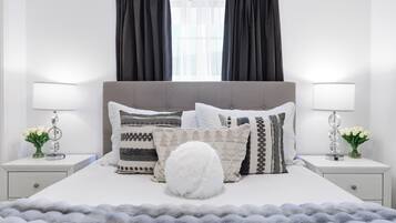 A neatly arranged bedroom with a large bed, two bedside tables, and a window with curtains.