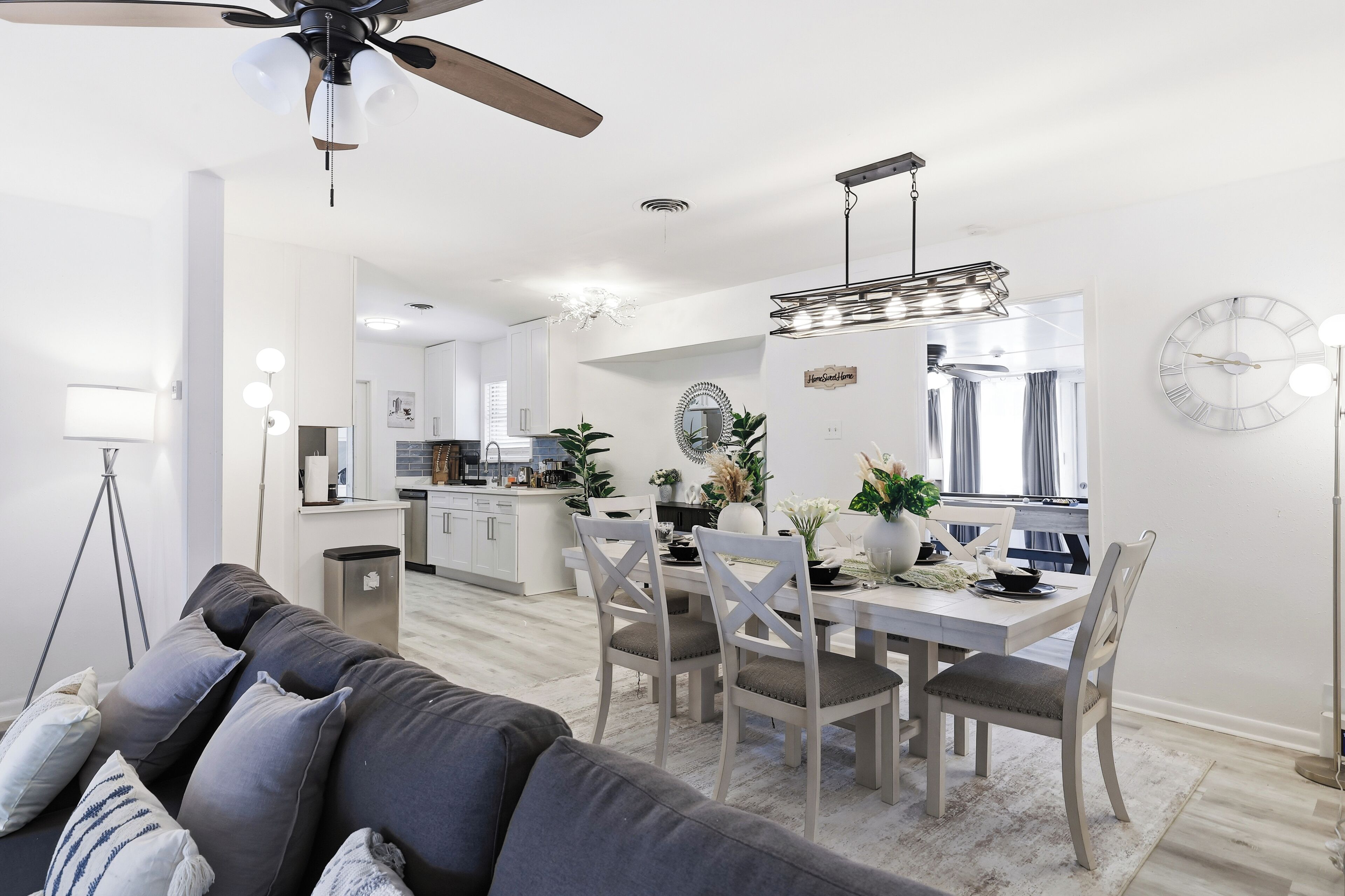 A modern kitchen with white cabinets, a dining table set for four, and a ceiling fan.