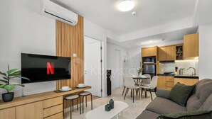 A modern living space with a flat-screen TV, a dining area, a kitchenette, and a sofa. - Casanoma by Kozystay - Paskal (Kota Bandung)