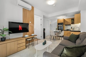 Ein modernes Wohnzimmer mit Flachbildfernseher, Essbereich, Küchenzeile und Sofa.