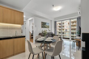 Eine moderne Küche mit Holzschränken, eine Essecke mit rundem Tisch und Stühlen sowie Blick auf ein Wohngebäude durch große Fenster.