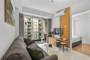 Un salon moderne avec un canapé, une table basse, un téléviseur et une vue sur un immeuble à travers de grandes fenêtres.