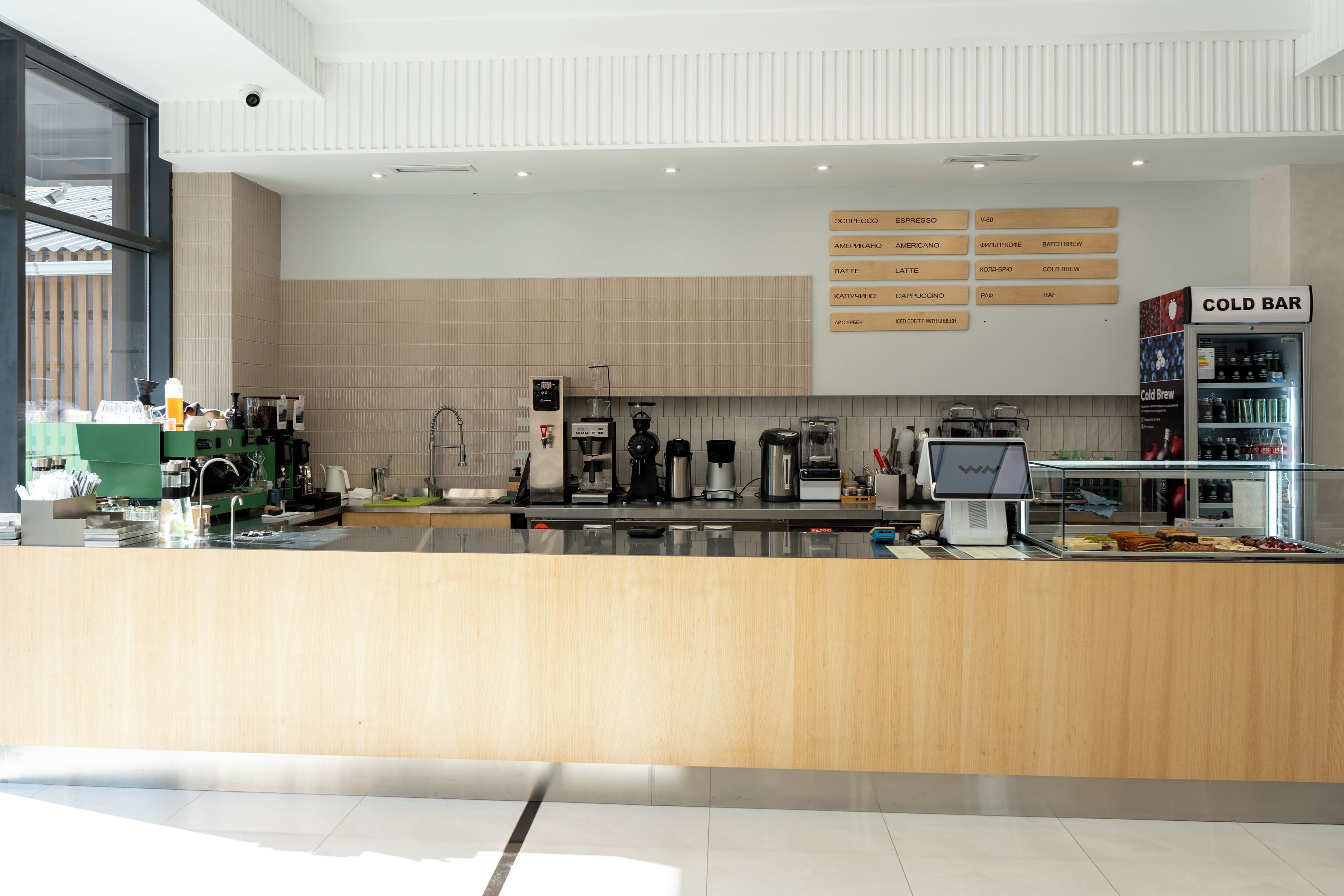 Interior moderno de una cafetería con mostrador de madera, máquinas de café y un panel con la carta de diferentes tipos de café.