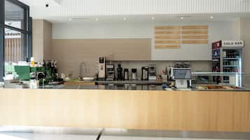 Interior moderno de una cafetería con mostrador de madera, máquinas de café y un panel con la carta de diferentes tipos de café.
