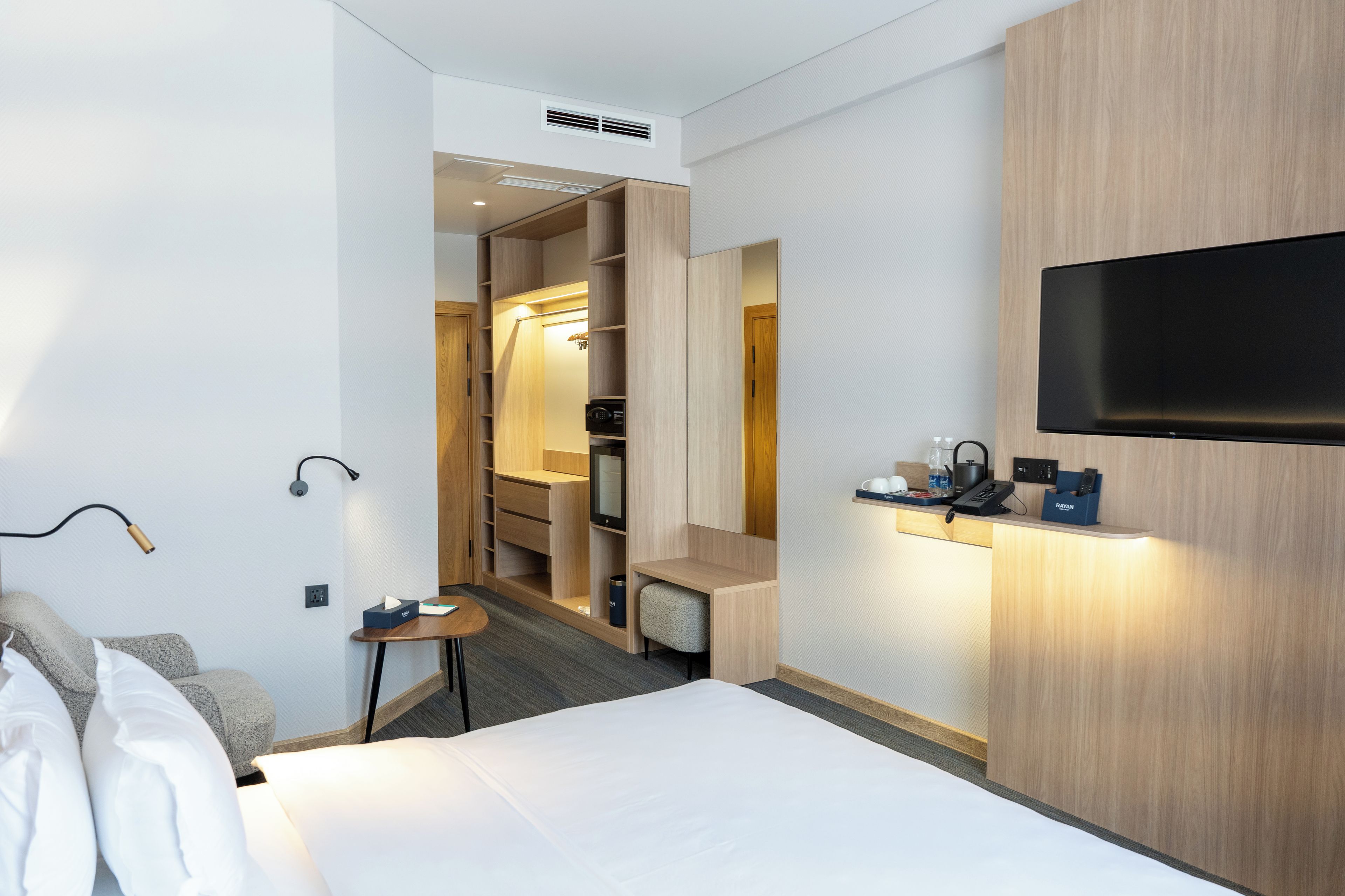 Quarto de hotel com cama, televisão na parede, escrivaninha com abajur e closet espaçoso.