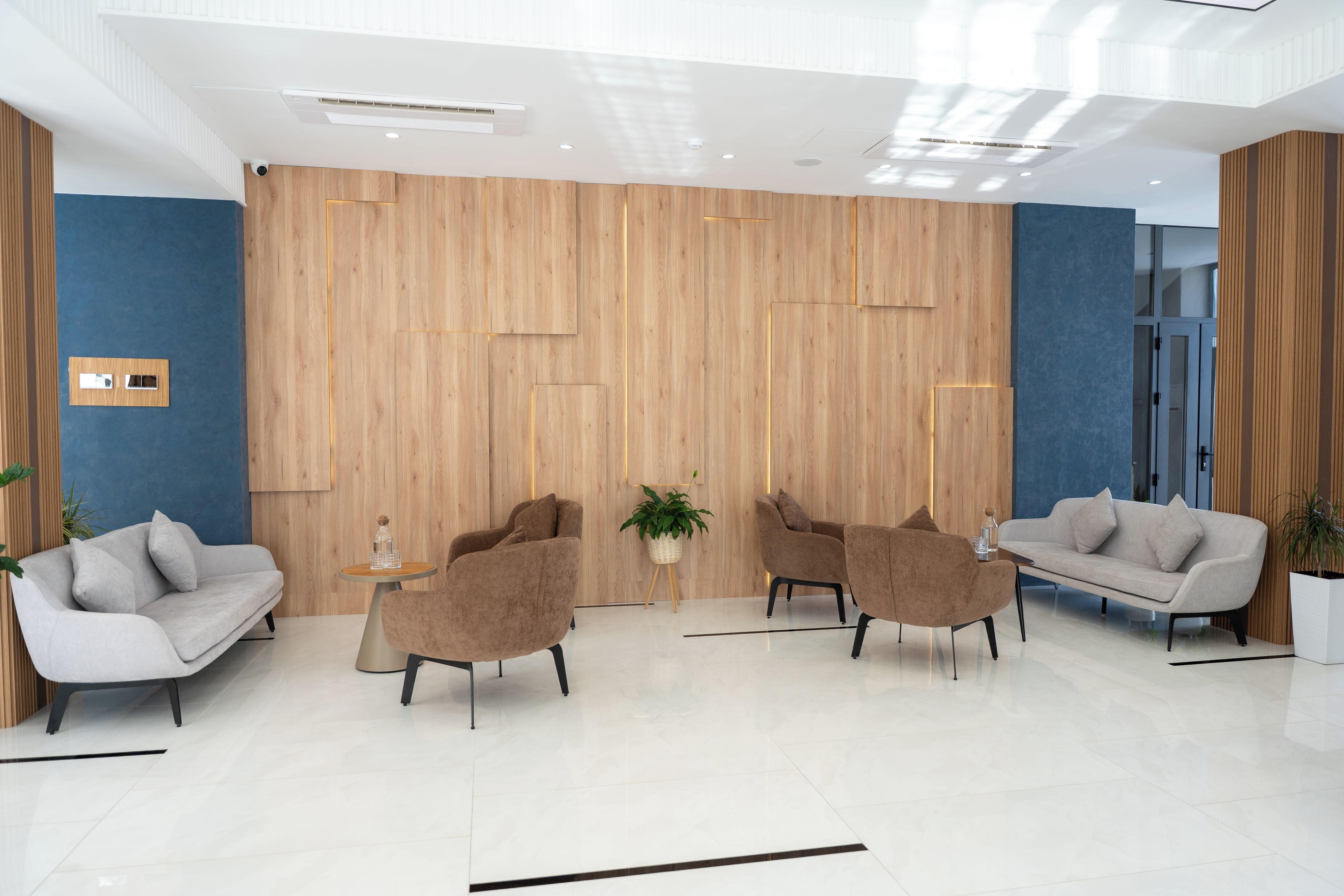 En moderne reception med en væg beklædt med træpaneler, to sofaer, et sofabord og en stueplante.