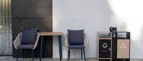 Twee stoelen met kussens, een bijzettafeltje en twee afvalbakken met recycling symbolen.