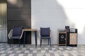Two chairs with cushions, a small table, and two waste disposal units with recycling symbols. - Rayan Regency Hotel  (Osh)