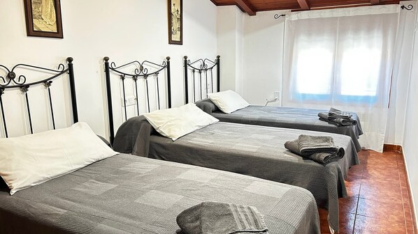 A hotel room with three single beds, each with a pillow and a folded towel.
