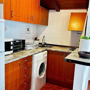 Kompakti keittiö, jossa on puukalusteet, sisäänrakennettu pesukone, mikroaaltouuni ja pesuallas.